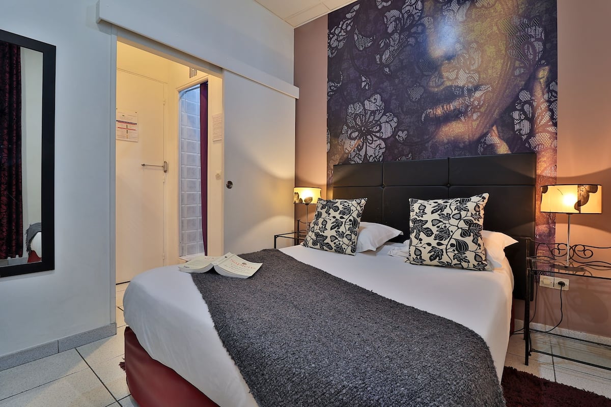 A neatly made bed with patterned pillows, a bedside lamp, and a wall with a floral design.