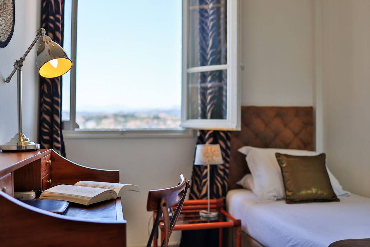 A hotel room with a desk, chair, bed, and a window with a view.