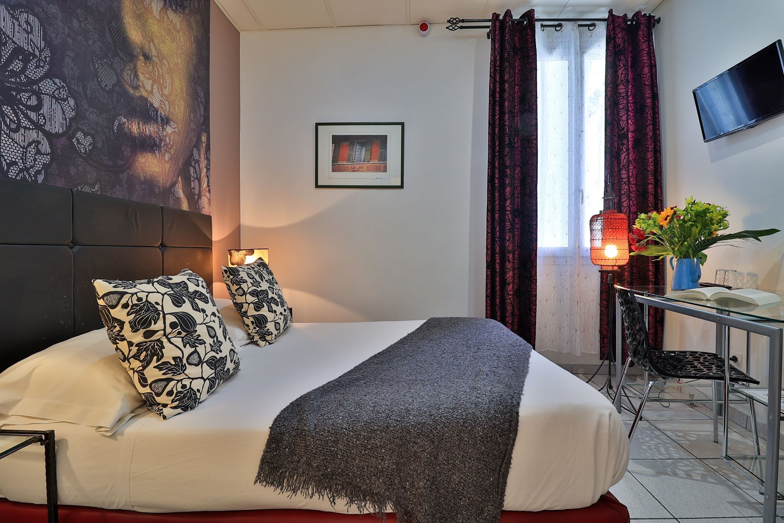 A neatly arranged hotel room with a large bed, a bedside table with a lamp, a chair, and a TV mounted on the wall.