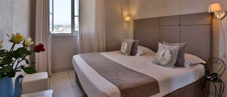 A bedroom with a large bed, a bedside table, a lamp, and a view of the city through a window.