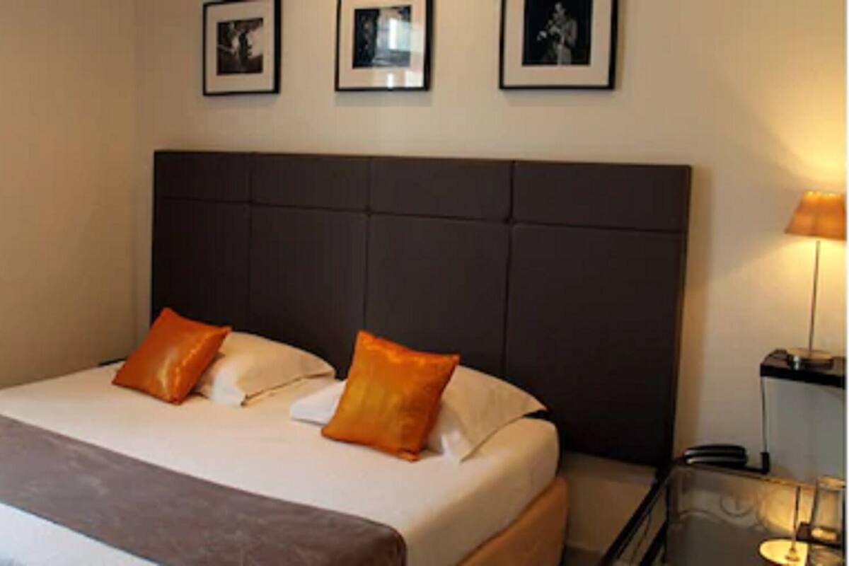 A hotel room with a large bed, two pillows, a headboard, and a bedside table with a lamp.
