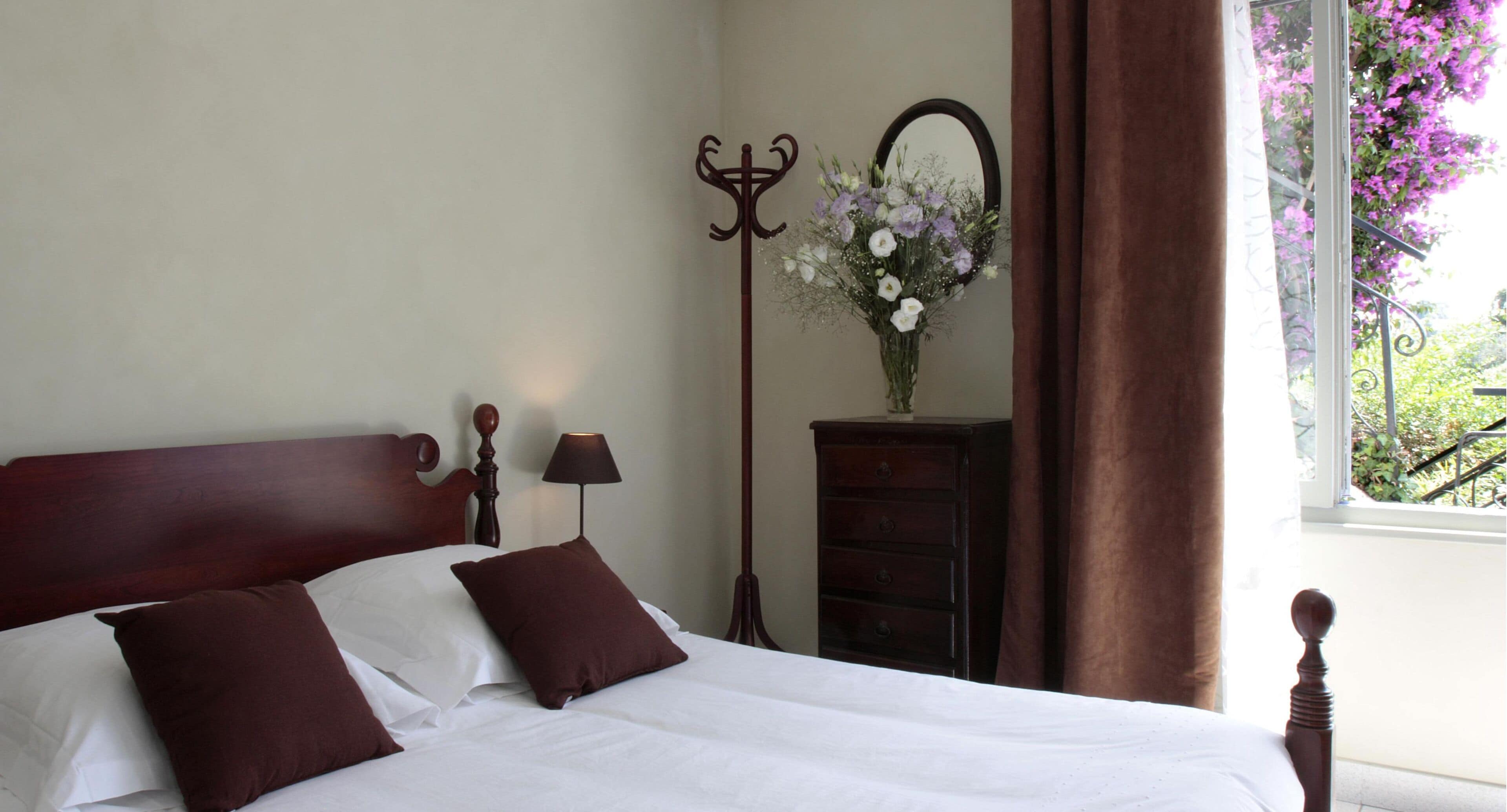A neatly made bed with two pillows, a bedside lamp, a dresser, and a mirror.