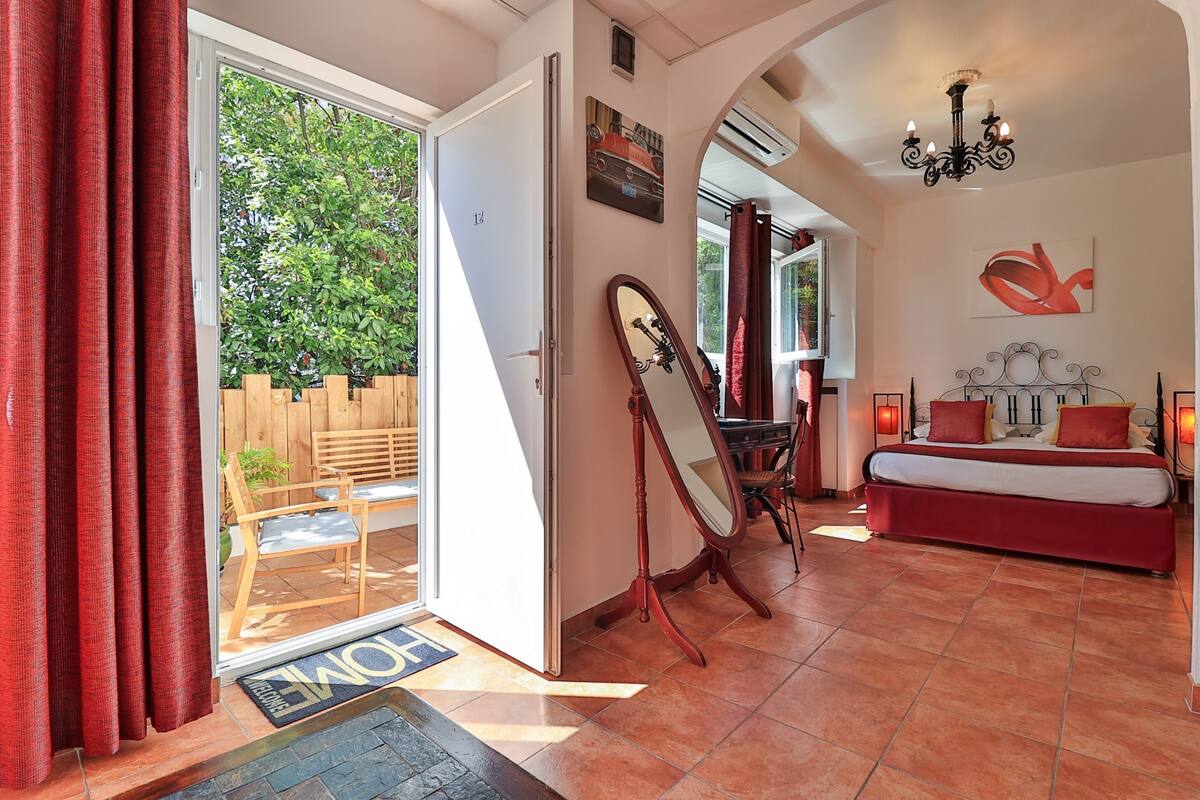 A spacious bedroom with a large bed, a sitting area with a table and chairs, a mirror, and a view of the outdoors.