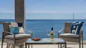 Een balkon met rieten stoelen, een glazen tafel, een fles wijn en een bord eten.
