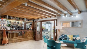 Een bar met een rustieke houten toonbank, een zithoek met teal stoelen en een bank, en een stenen muur met een klok.