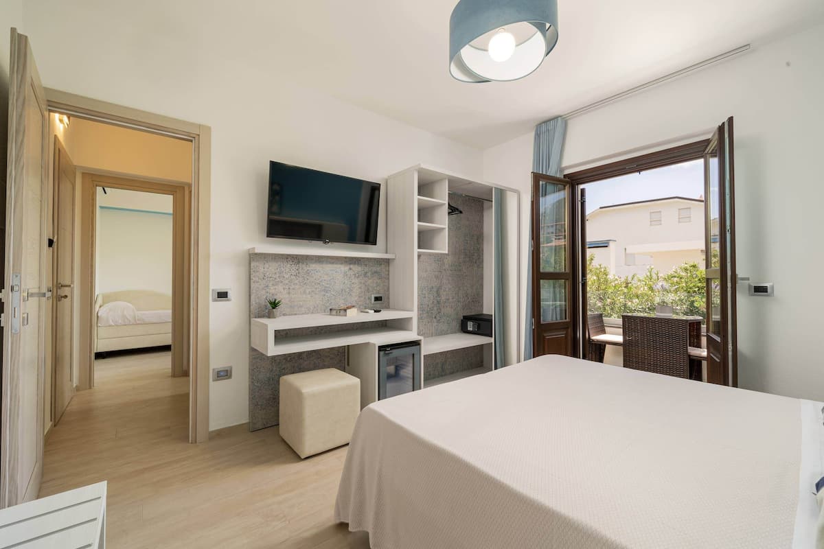 Ein modernes Hotelzimmer mit Bett, Schreibtisch, Fernseher und einer kleinen Küchenzeile.