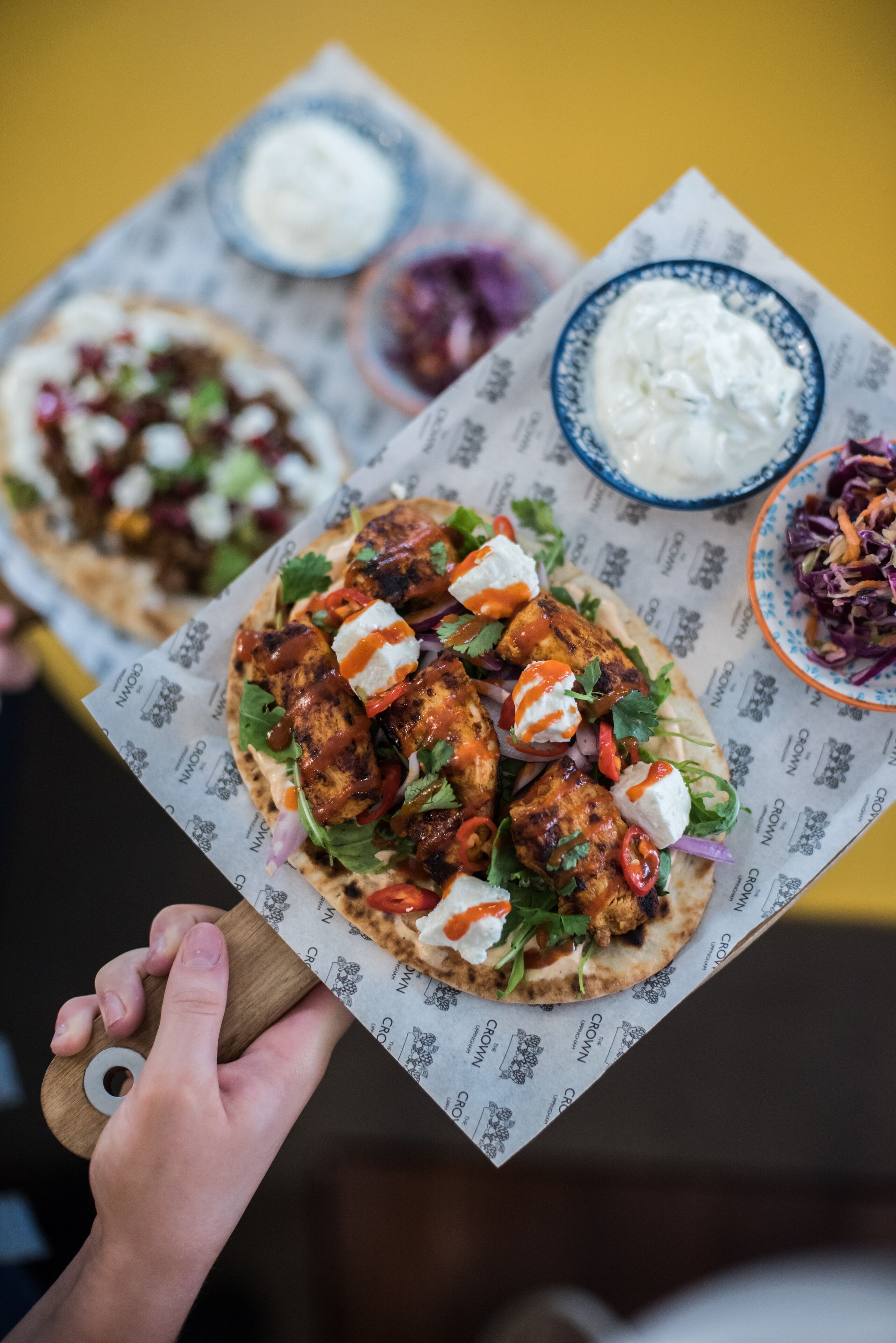 A person holding a food tray with a grilled chicken wrap, a side salad, and a bowl of sauce.