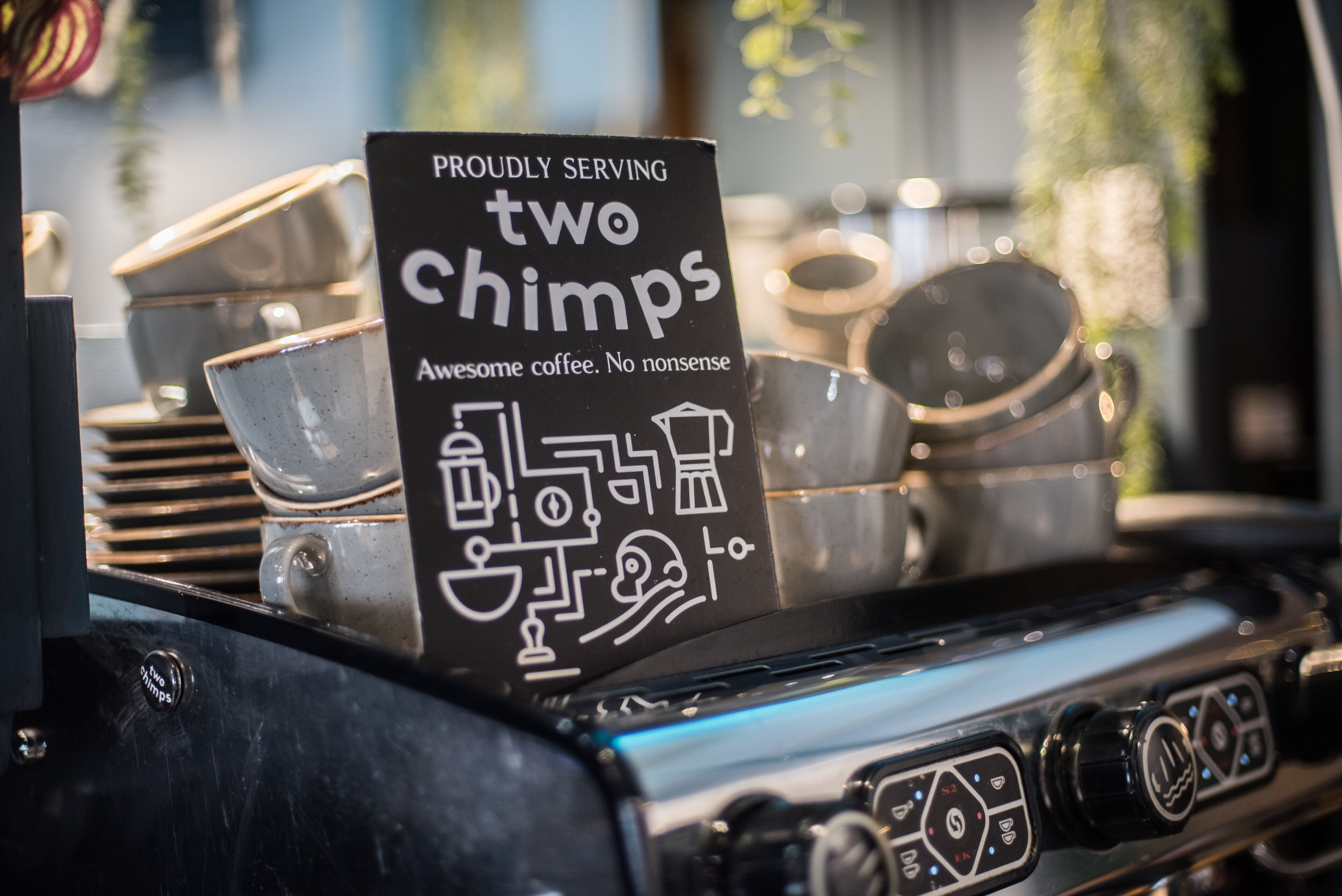A coffee machine with a sign that reads "PROUDLY SERVING two chimpps Awesome coffee. No nonsense."