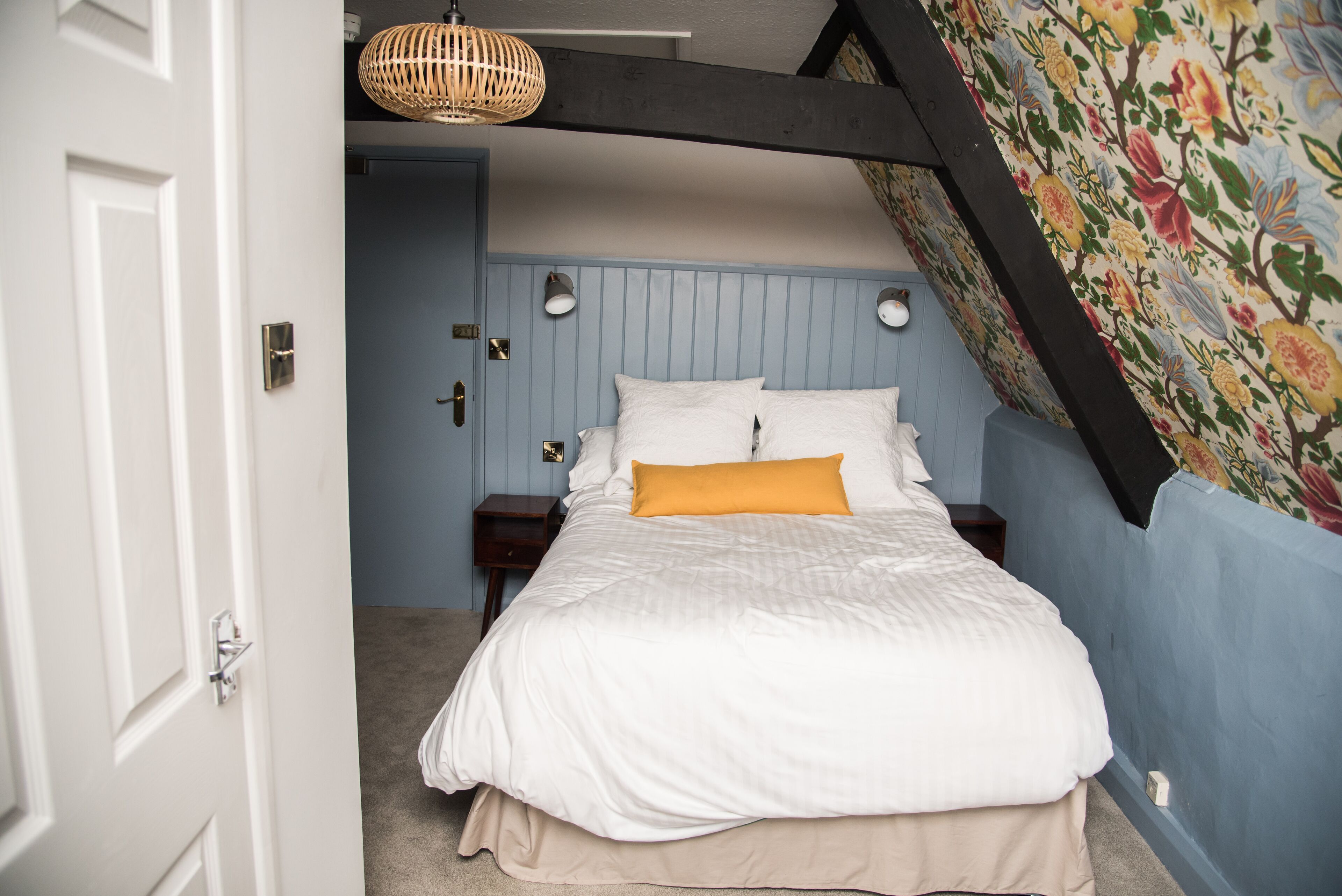 A bedroom with a bed, a nightstand, a wall-mounted lamp, and a door.