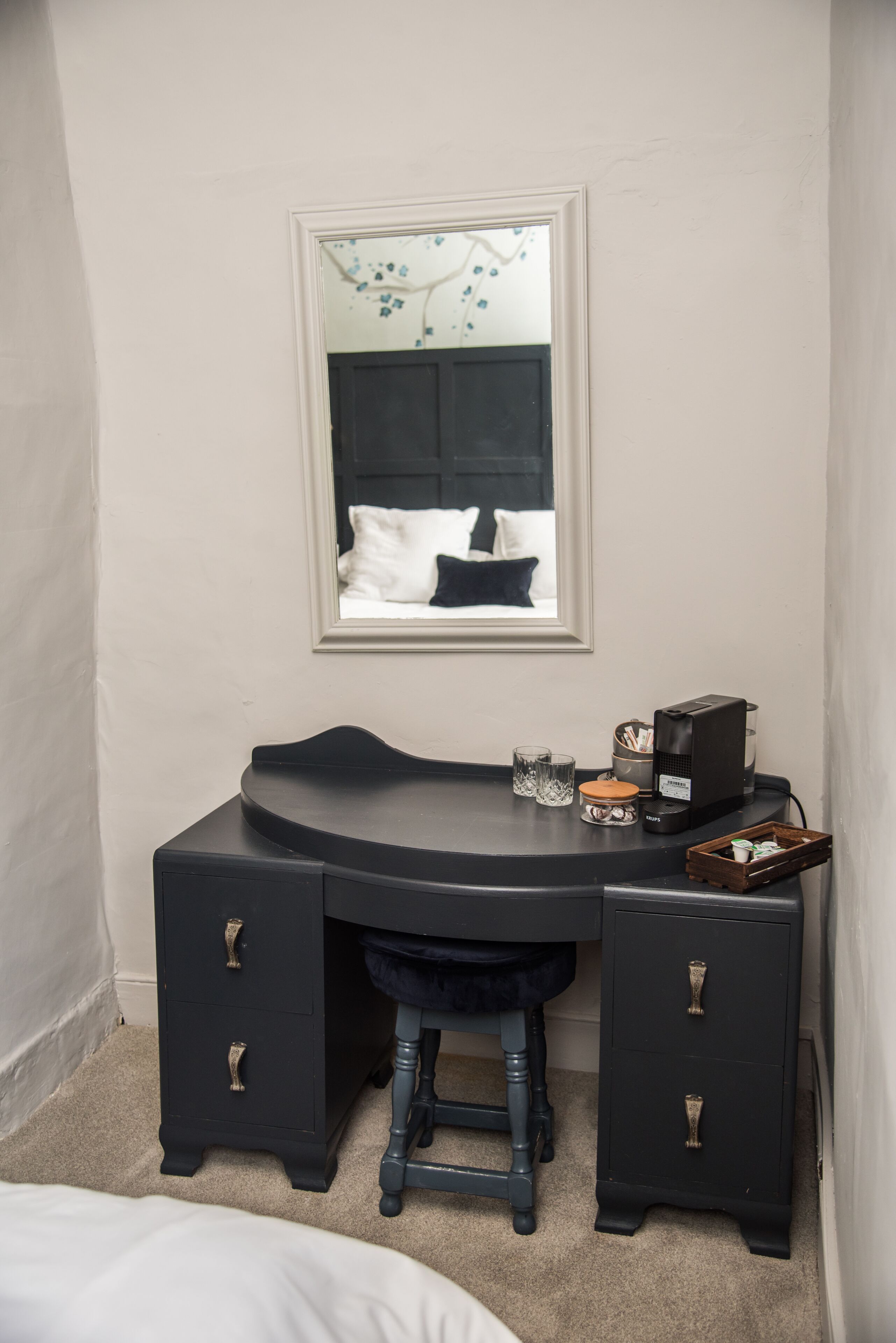A dark-colored vanity with a mirror above it, a stool, and a small cabinet with drawers.