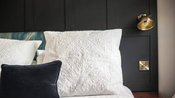 A neatly made bed with white and dark pillows, a dark headboard, and a brass wall sconce.