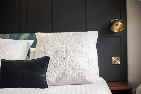 A neatly made bed with white and dark pillows, a dark headboard, and a brass wall sconce.