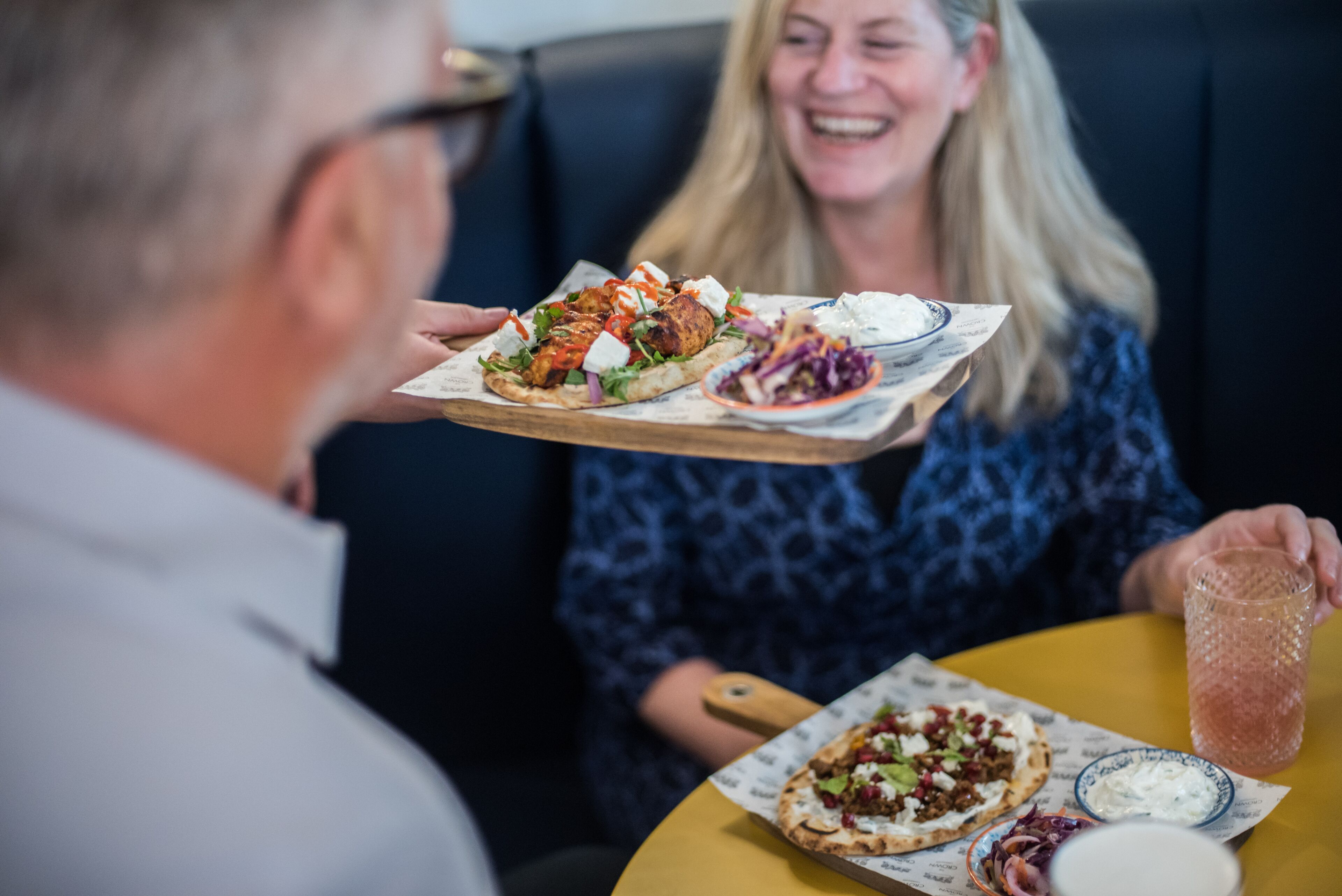 A dining table with a tray of food, a glass of drink, and a bowl of sauce.