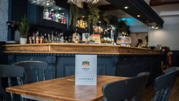 A bar area with a wooden table and chairs, a sign indicating 'CROWN COCKTAILS', and a bar stocked with bottles and glasses.