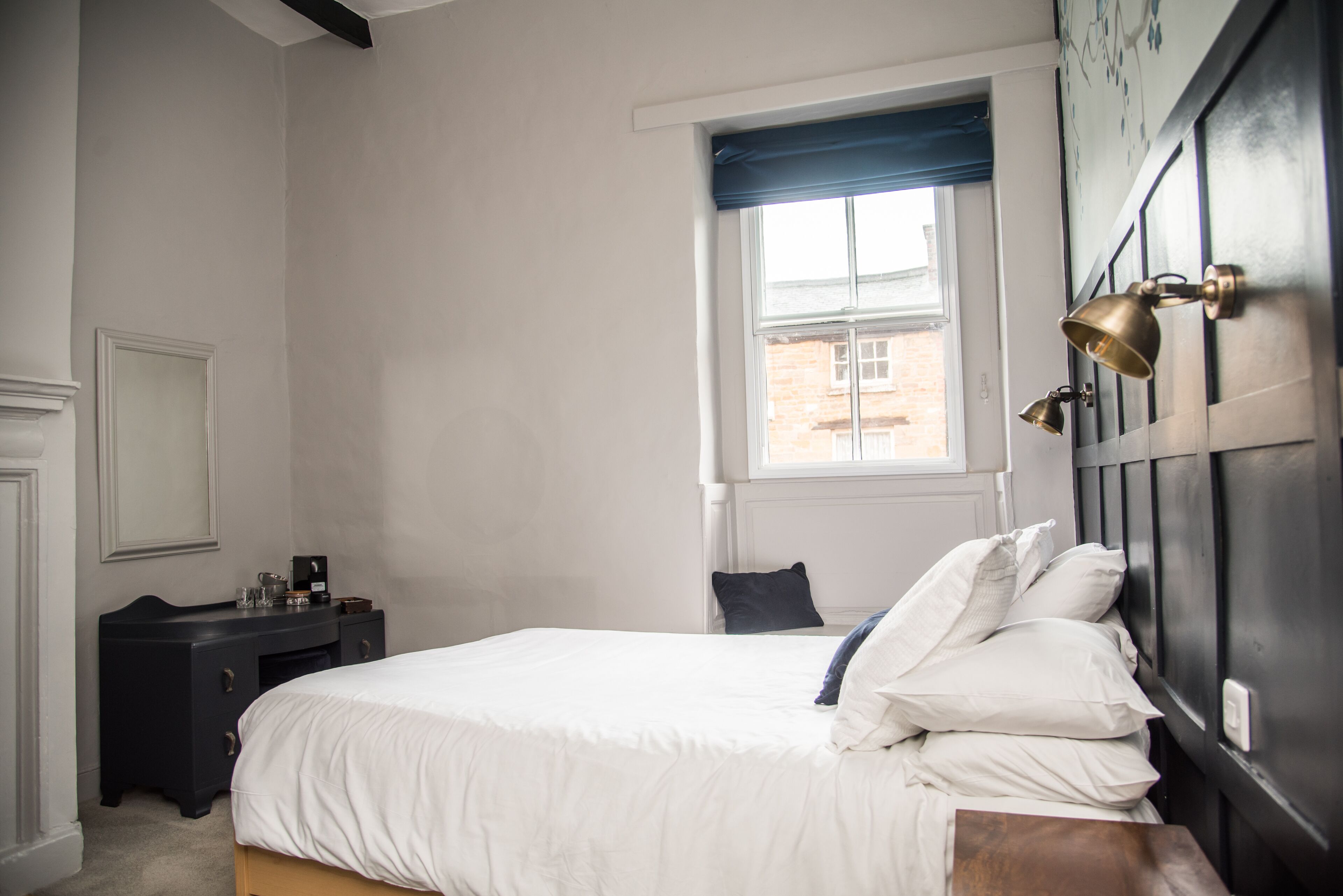 A bedroom with a bed, a dresser, a window, and a wall-mounted light fixture.