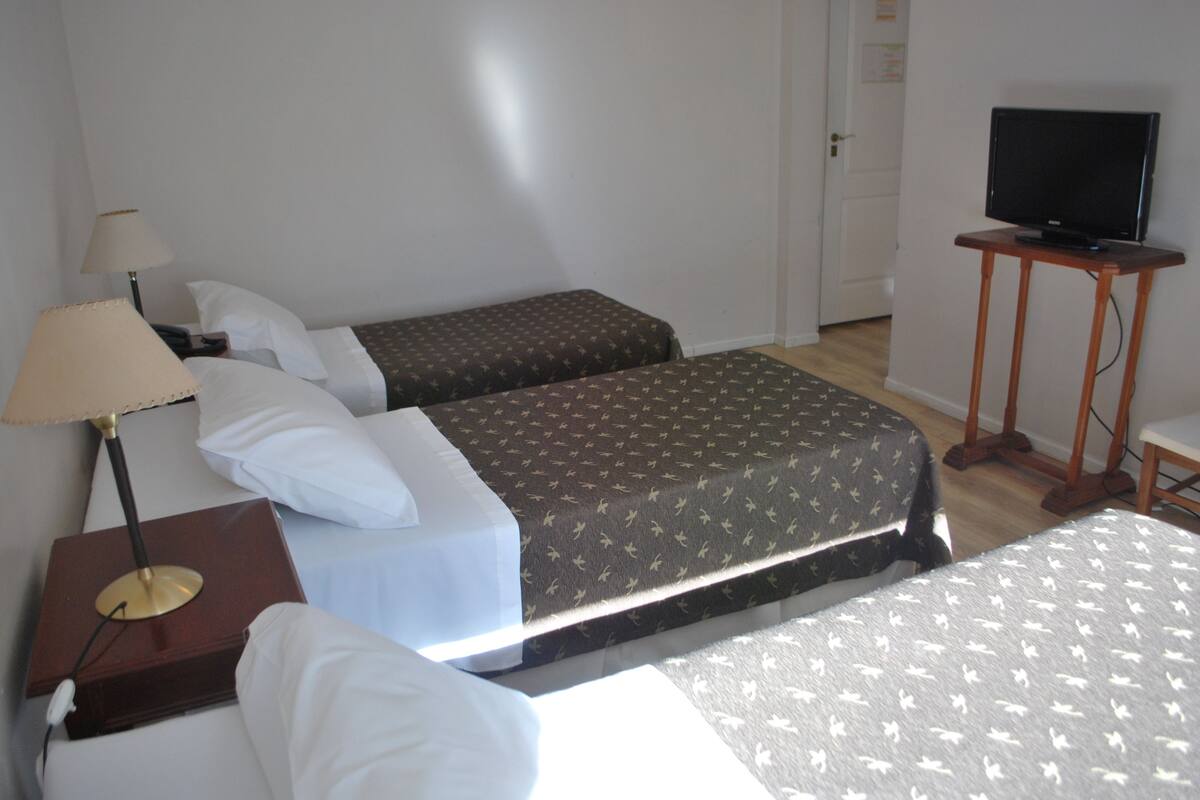 Una habitación de hotel con dos camas, un televisor sobre un soporte de madera y una lámpara en una mesita de noche.