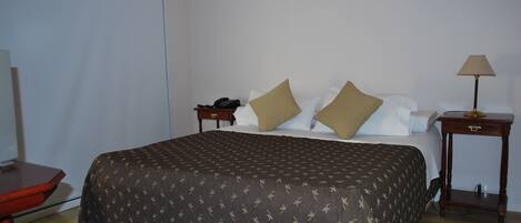 A neatly made bed with a patterned bedspread, a bedside table with a lamp, and a telephone on the nightstand.