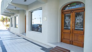 Entrada de hotel con un paseo de baldosas, amplias ventanas y puertas dobles de madera con letrero del hotel.