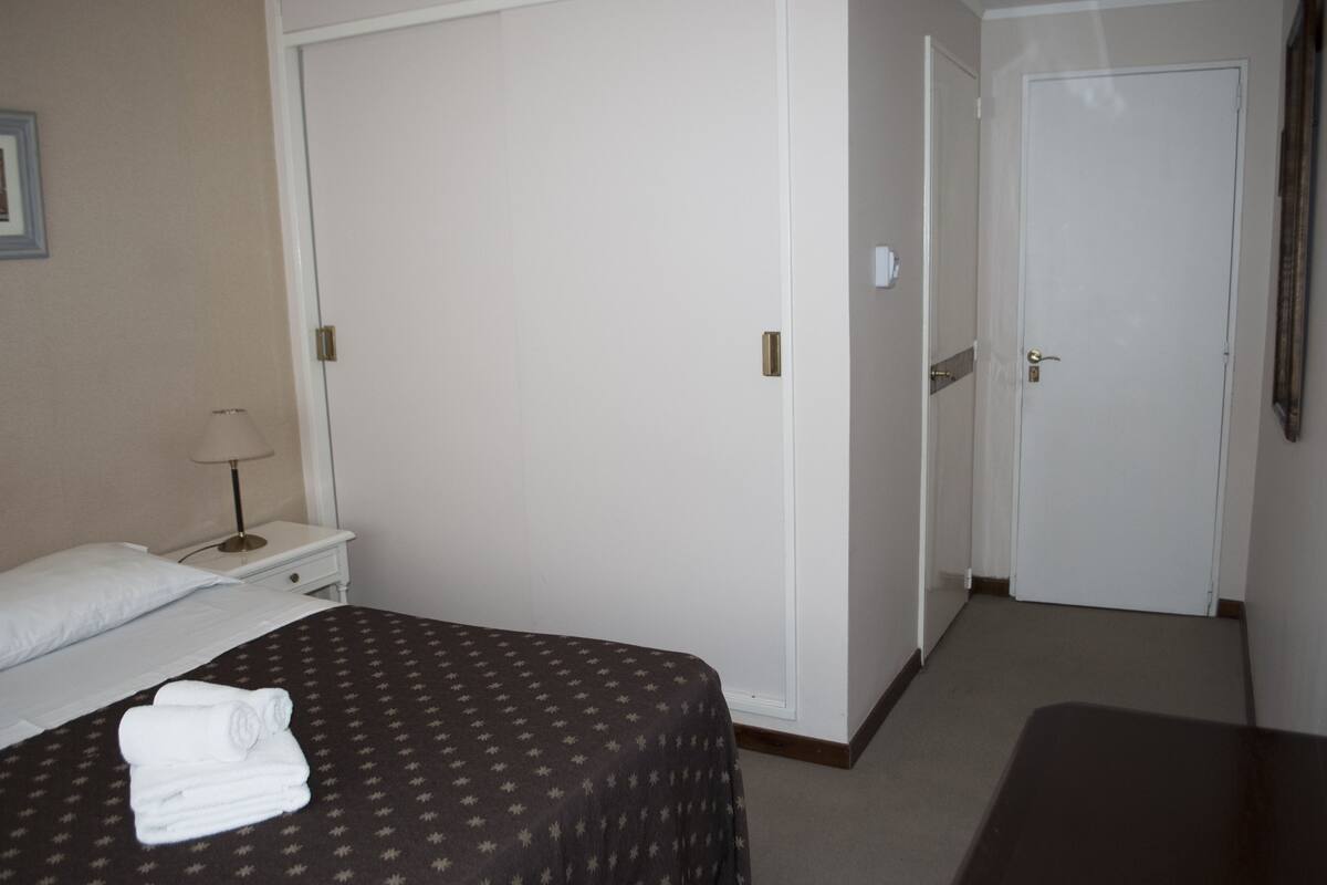 Una habitación de hotel con cama, mesita de noche, lámpara y puerta.