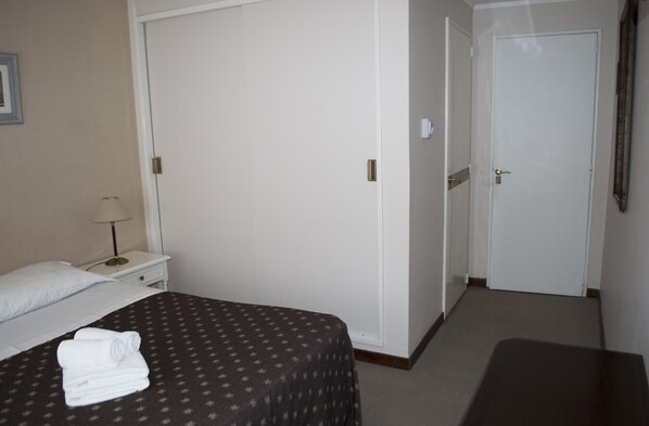 A hotel room with a bed, a nightstand, a lamp, and a door. - Gran Madryn (Puerto Madryn)