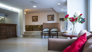 Un salón amplio con un sofá, dos sillones, una mesa de centro y un jarrón con flores.