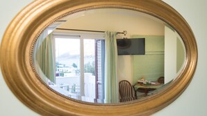 Une pièce dotée d’un grand miroir, d’un téléviseur fixé au mur, d’une table à manger avec des chaises, et offrant une vue sur l’extérieur grâce à une fenêtre agrémentée de rideaux.