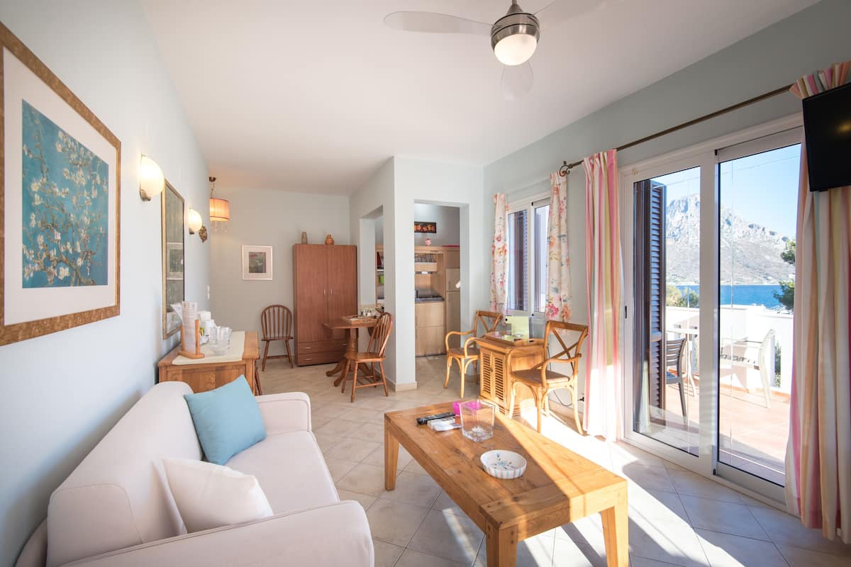 Una sala de estar con un sofá, una mesa de centro de madera y un comedor con sillas y una mesa. Se observa una cocina al fondo y una puerta corrediza de vidrio que da a un patio exterior.