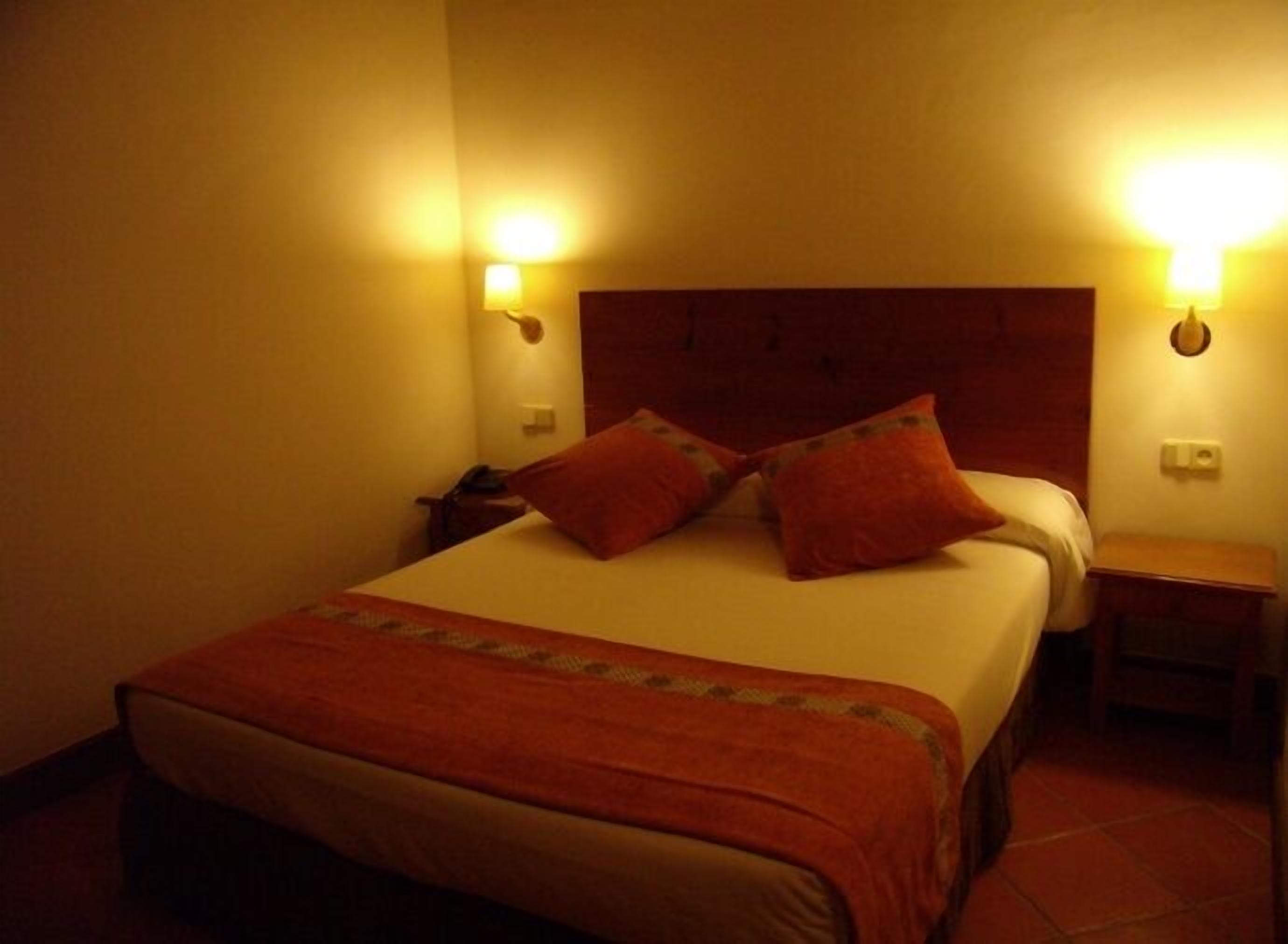 Habitació d'hotel amb un llit gran, dues taules de nit i dues làmpades penjades a la paret.