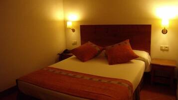 Habitació d'hotel amb un llit gran, dues taules de nit i dues làmpades penjades a la paret.