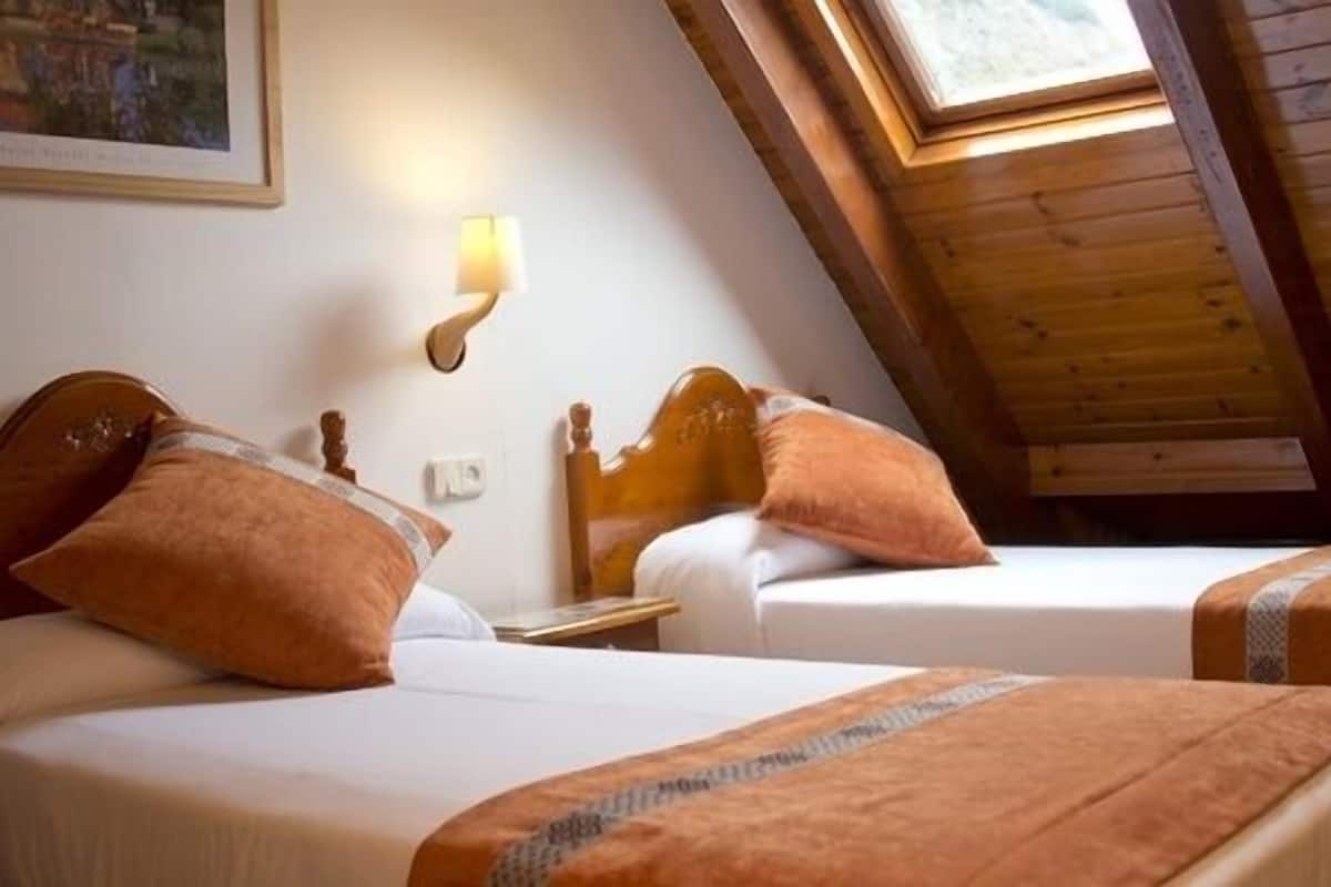 Une chambre avec deux lits, des têtes de lit en bois, une table de chevet, une lampe fixée au mur et un puits de lumière.