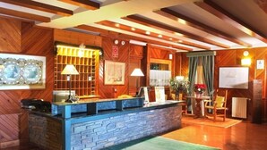 A reception area with a stone counter, wooden paneling, and a green rug. - Hotel y Apartamentos Vilagaros (Naut Aran)