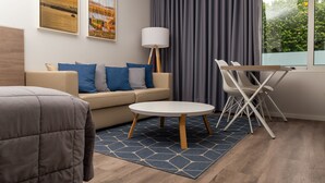 A modern hotel room with a sofa, a round table, a lamp, and a view of the outdoors. - Do Parque - Viana do Castelo (Viana do Castelo)