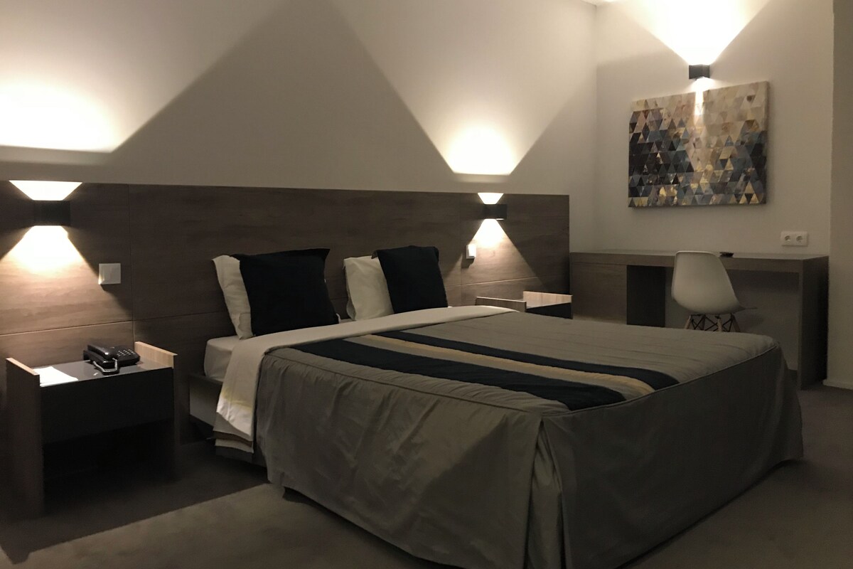 Ein modernes Hotelzimmer mit einem großen Bett, Nachttischlampen, einem Schreibtisch und einem Bild an der Wand.