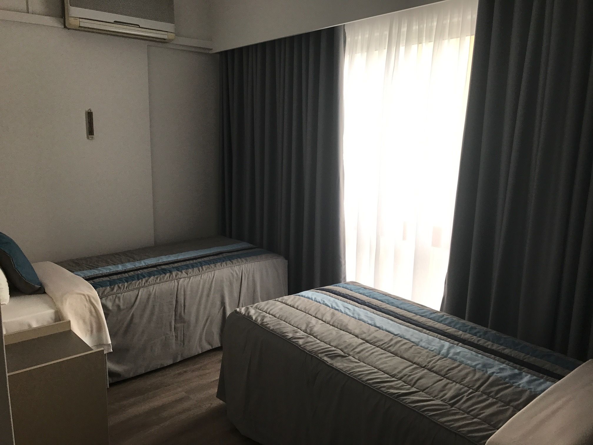 A small, single-bed room with a bed, a bedside table, and a window with curtains.