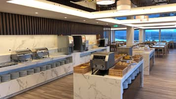 A modern buffet setup with self-service stations, a coffee machine, and a variety of food items.