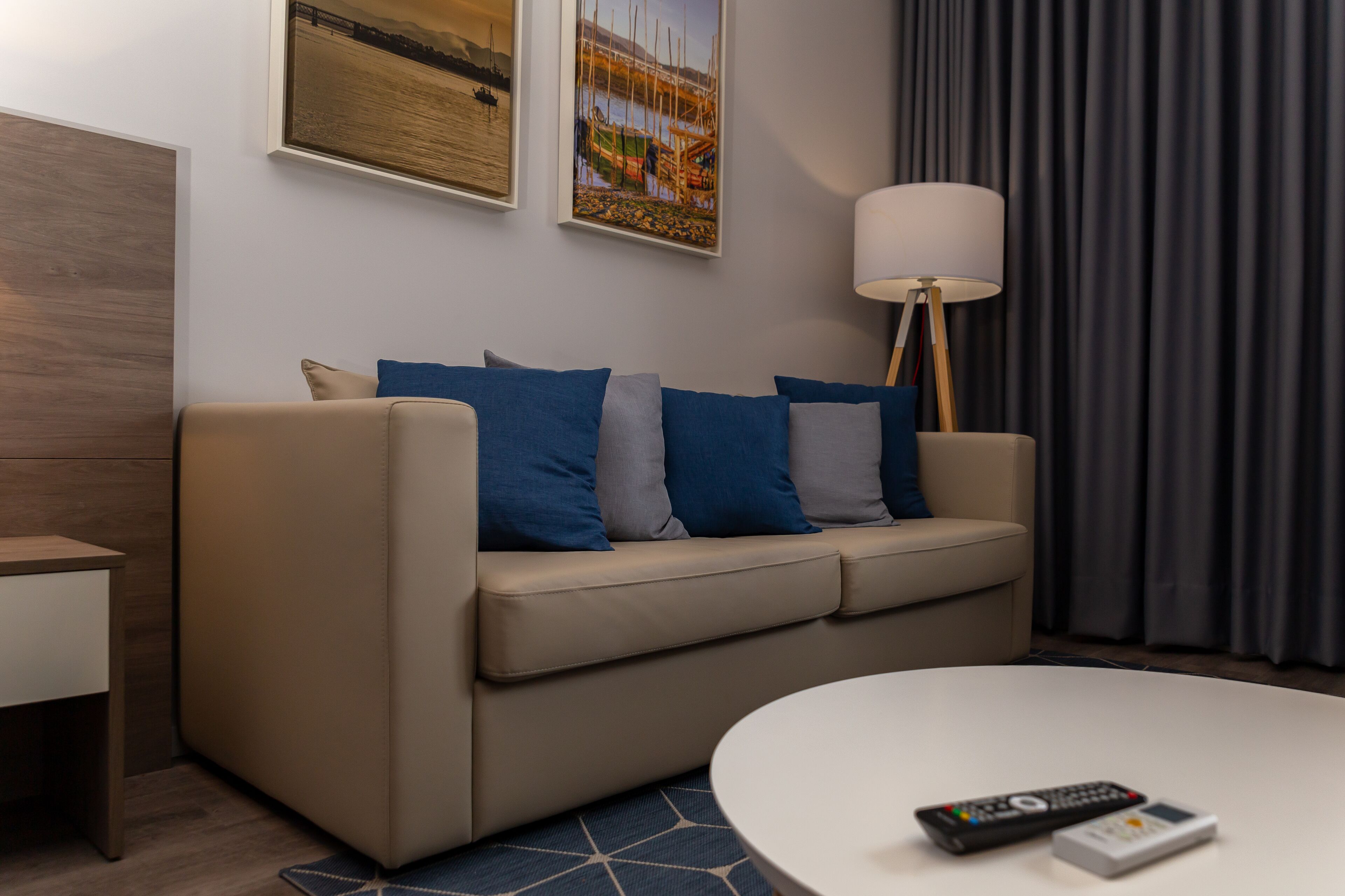 Una sala de estar moderna con un sofá color beige, cojines azules y grises, una mesita de centro blanca y un control remoto.