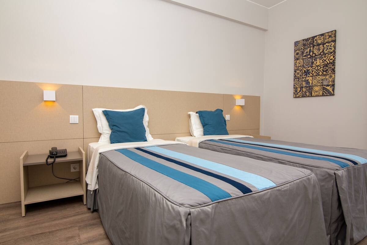 A hotel room with two single beds, each with a pillow and a bedside table.