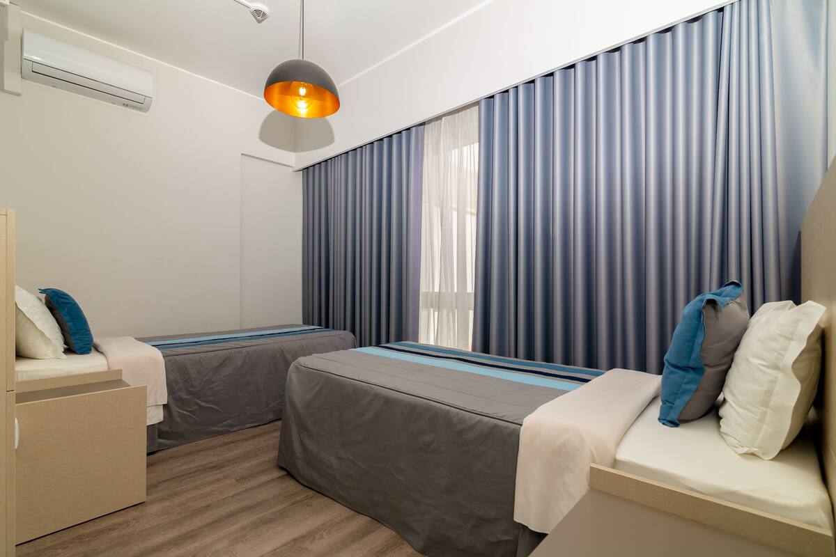 A hotel room with two beds, a wardrobe, and a ceiling-mounted air conditioner.