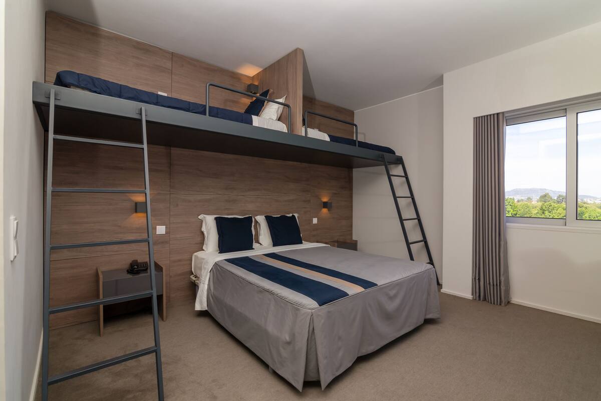A bunk bed room with a ladder, a small desk, and a window with a view.