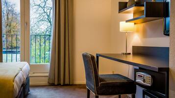 A hotel room with a bed, a desk with a chair, a lamp, and a wall-mounted TV.