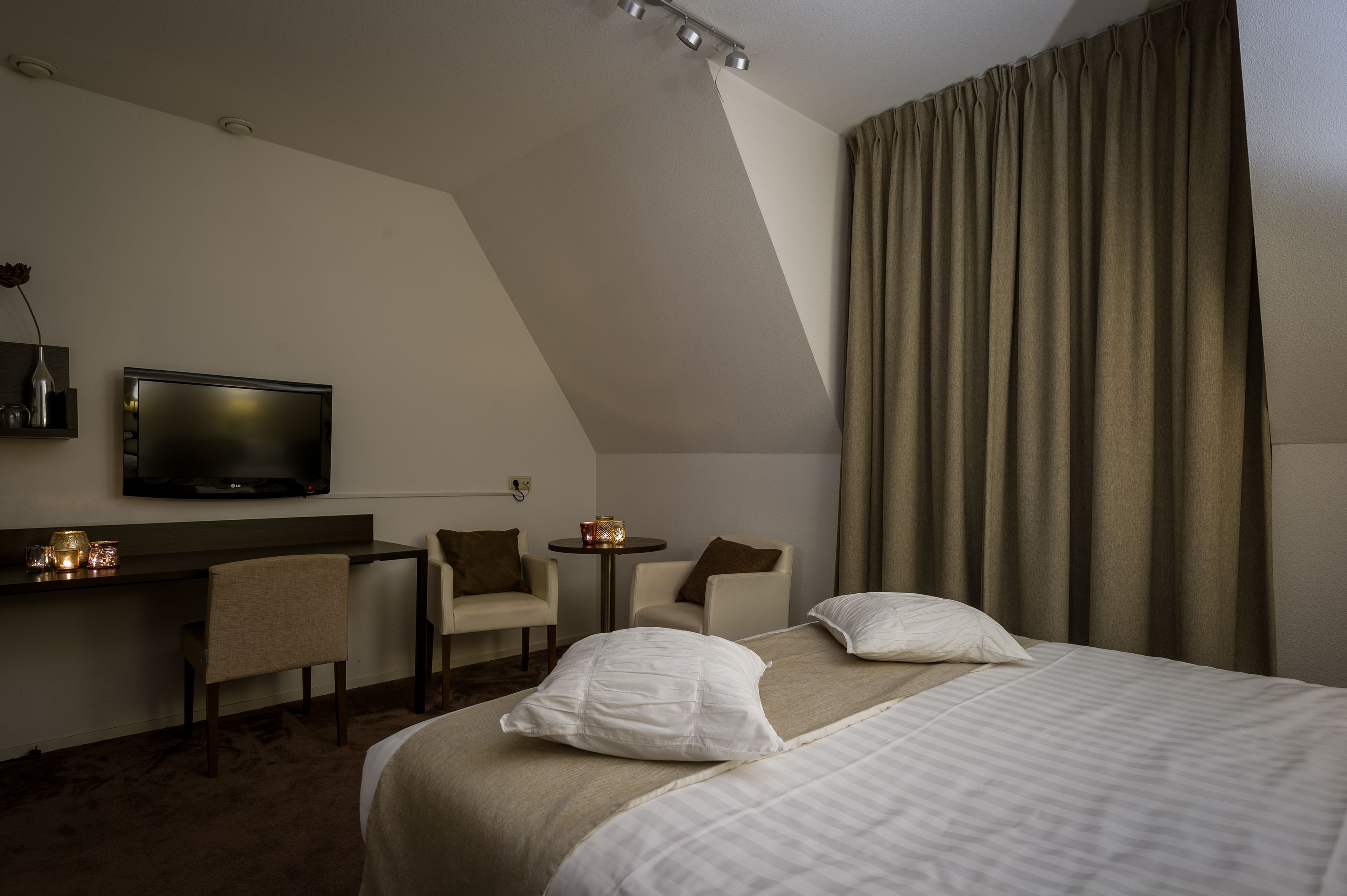 Habitación de hotel con cama, dos sillas, escritorio, televisor y ventana con cortinas.