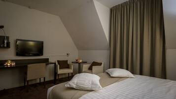 Habitación de hotel con cama, dos sillas, escritorio, televisor y ventana con cortinas.