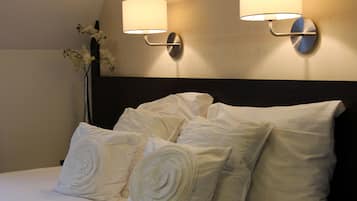 Een net opgemaakt bed met opgerolde kussens en twee wandlampen.