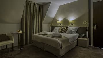 Una habitación de hotel moderna con una cama grande, una mesita de noche con lámpara, una pequeña mesa auxiliar y un rincón de descanso con un sillón.