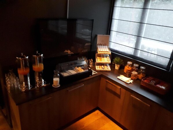 Una barra de desayuno con una vitrina de vidrio, una bandeja escalonada de postres y una ventana con persianas.