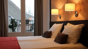 Una habitación de hotel con cama, dos lámparas de pared y vistas a un edificio a través de una ventana.