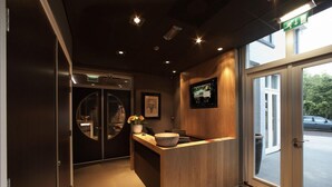 Un área de recepción con un mostrador de madera, una pantalla digital y una puerta de vidrio que da al exterior.
