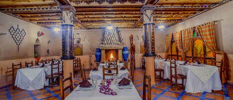 Un comedor con mesas dispuestas para una comida, una chimenea en el centro y un suelo con estampado.