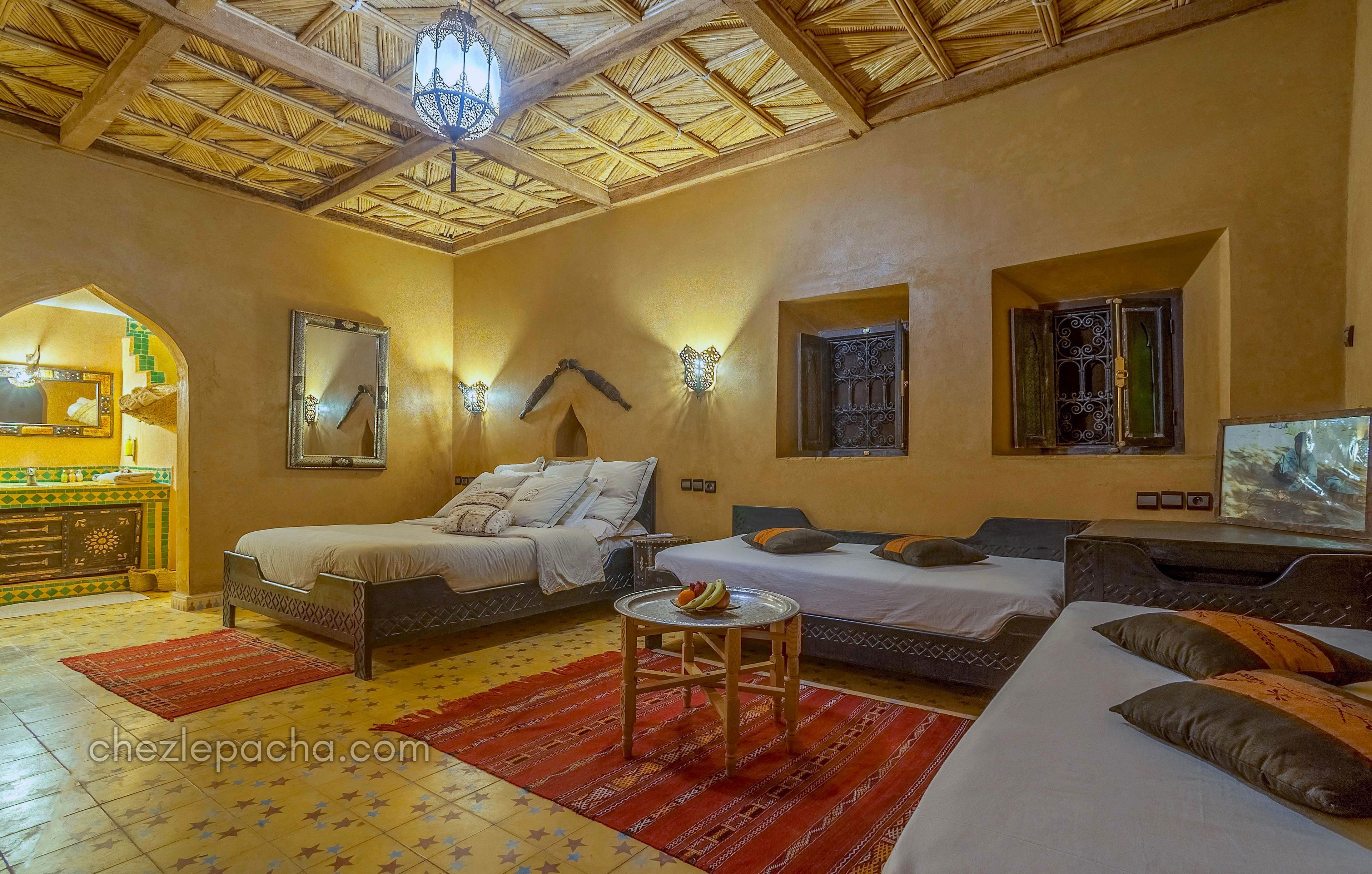 A room with two beds, a sofa, a small table with fruit, and decorative wall sconces.