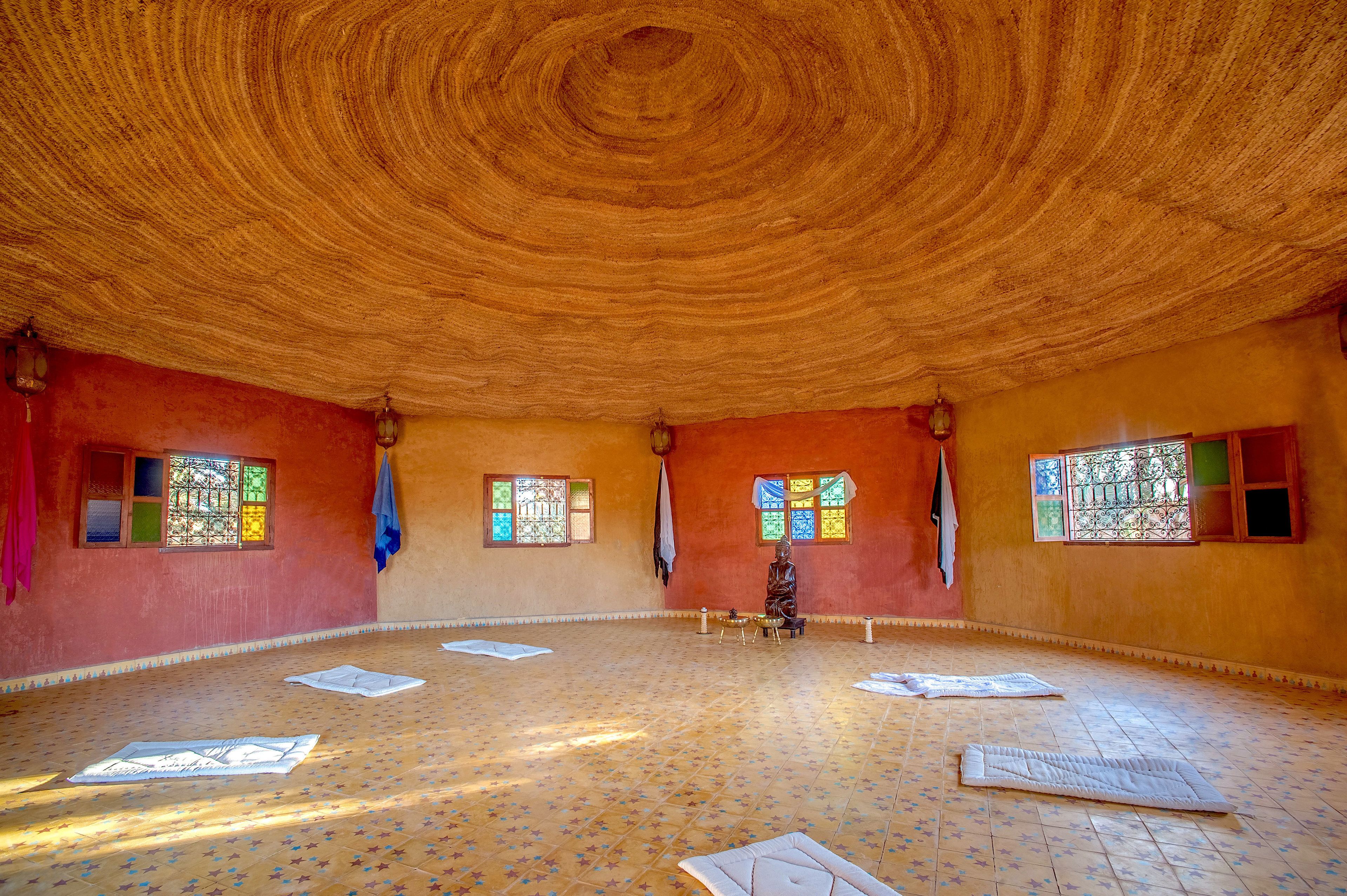 A room with a circular wooden ceiling, patterned floor, and windows with bars.